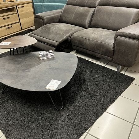 Ein graues Sofa steht hinter einem dunklen Teppich mit grauem Couchtisch