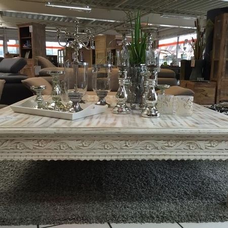 Ein rustikaler, weißer Couchtisch mit Deko steht auf einem Teppich