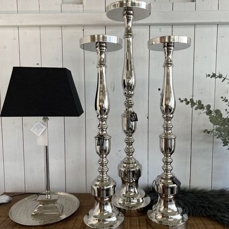 3 silberne hohe Kerzenhalter stehen neben einer Lampe mit schwarzem Lampenschirm